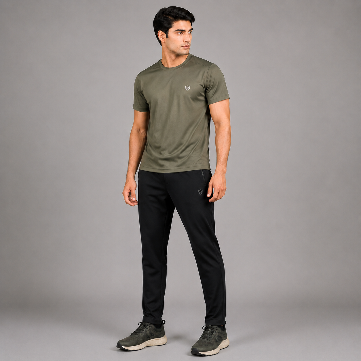 A man modeling an olive green short-sleeve athletic t-shirt and black athletic pants against a solid gray studio background.