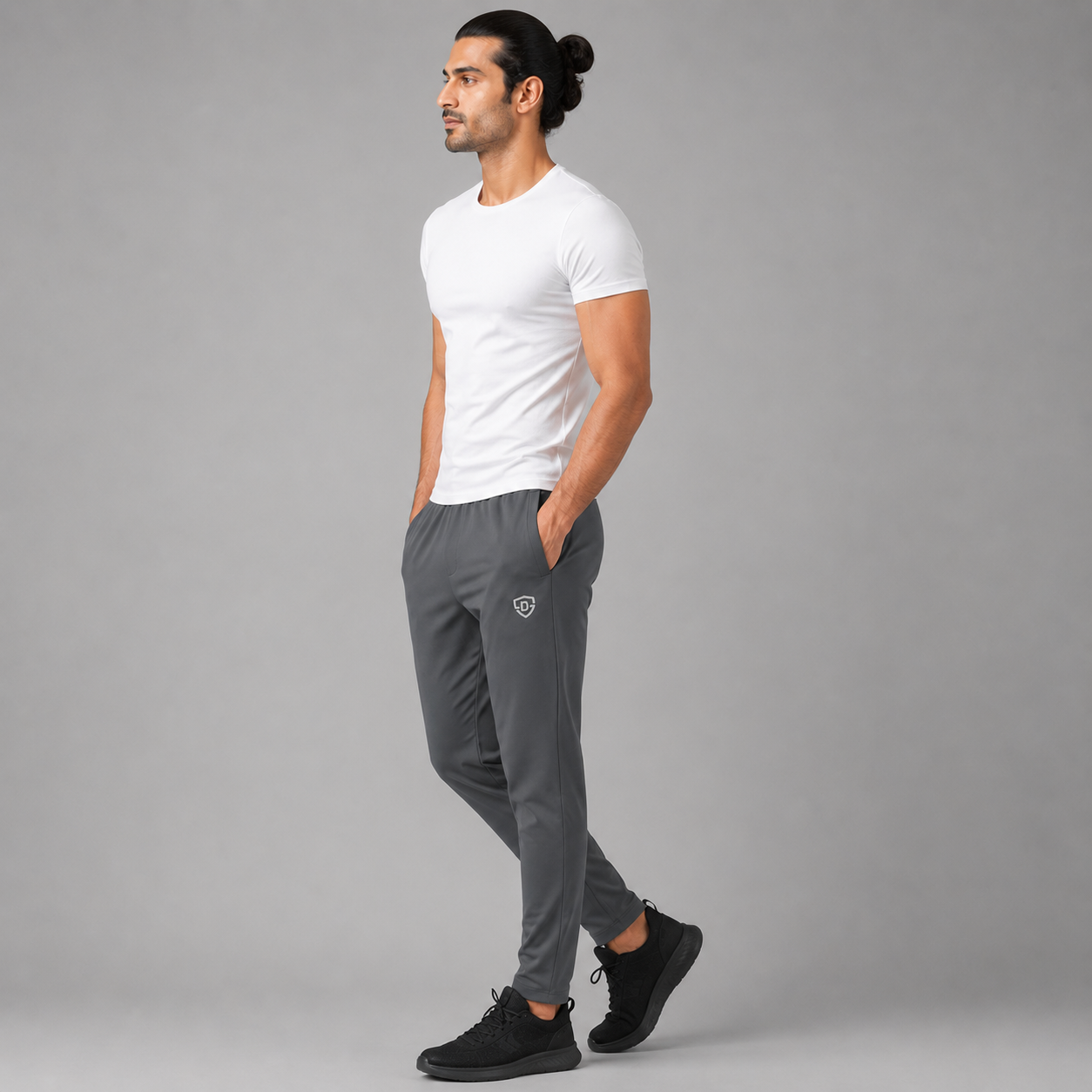 A man in a white t-shirt and gray jogger trousers / sweatpants walking in profile against a solid gray studio background.